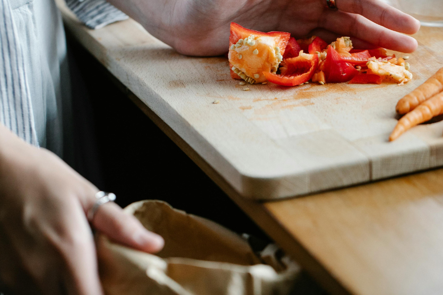 person scraping vegetable scraps on a wooden chopping board into brown paper bag